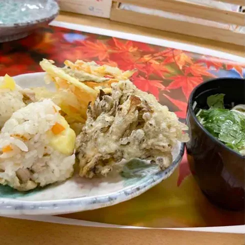 混ぜご飯のおにぎり、天ぷら、お吸い物などが美しく盛り付けられている
