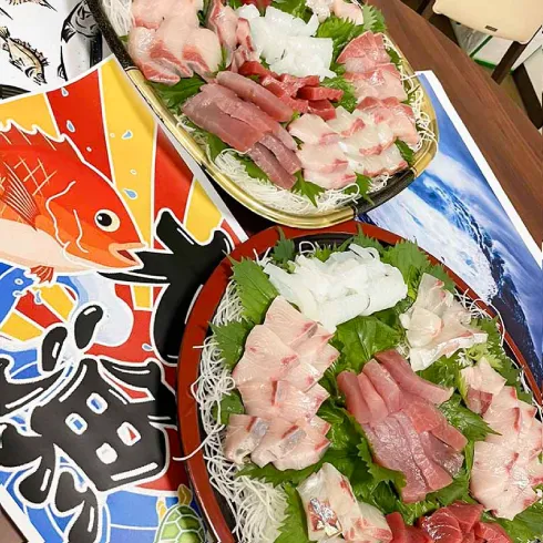 様々な魚種のお刺身が盛り付けられている。机の上には大漁旗